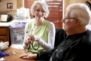 A palliative care nurse talks with male patient at his home.